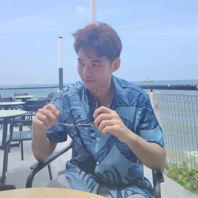 Gan Zhi Ken seated by the sea, holding a pair of glasses